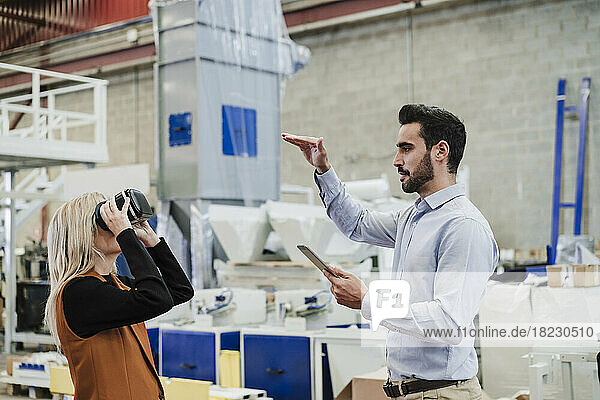 Businessman gesturing with colleague wearing virtual reality simulator at factory