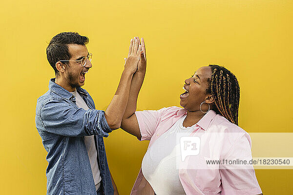 Cheerful man and woman giving high-five to each other in front of yellow wall