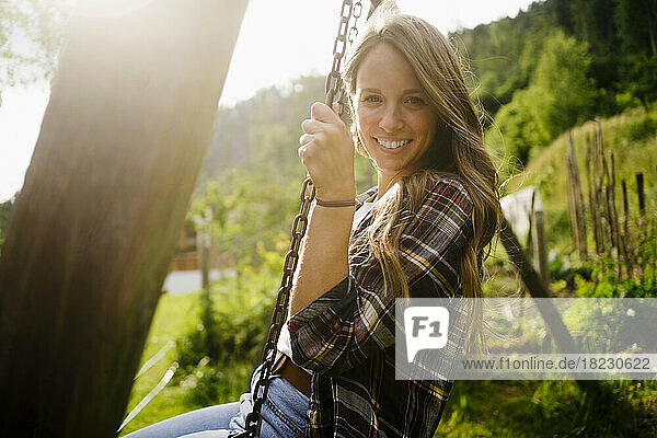 Happy young woman sitting on swing in garden