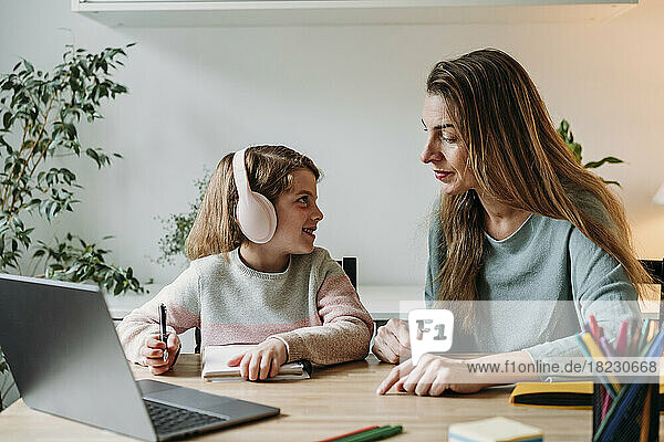 Mother helping girl in study sitting with laptop on table at home