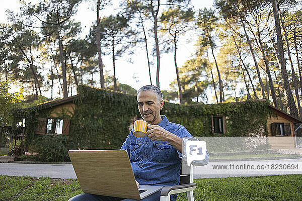 Mature man drinking coffee and using laptop outdoors