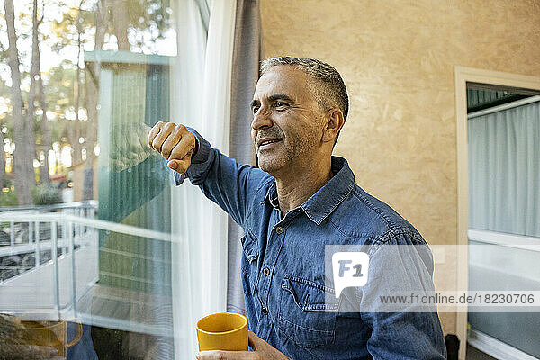 Mature man holding coffee cup at home looking out of window