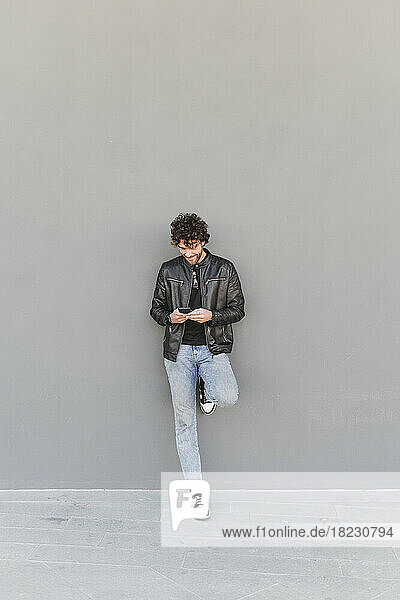 Man using smart phone leaning on gray wall