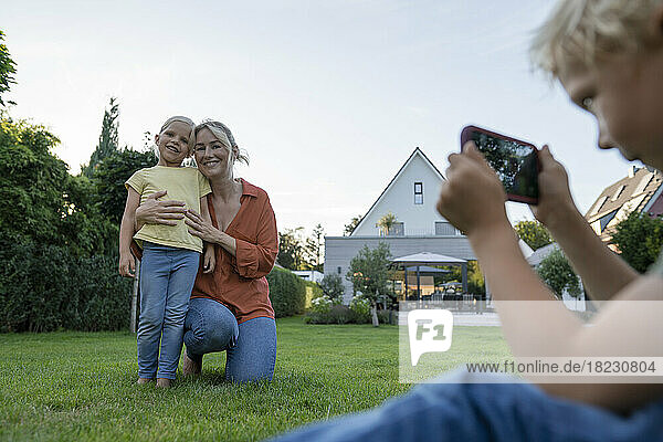 Junge fotografiert Mutter und Schwester per Smartphone im Garten