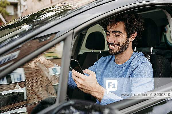 Smiling man using smart phone sitting in car