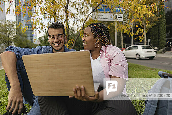 Happy woman with man using laptop in front of tree