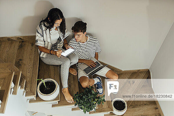Geschwister lernen gemeinsam über Tablet-PC und sitzen zu Hause auf der Treppe