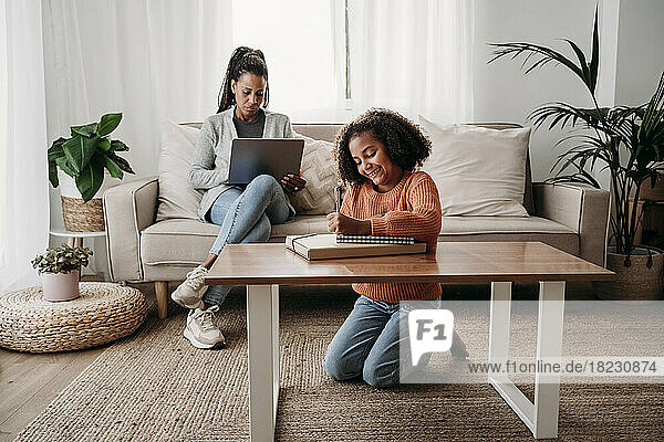 Glückliches Mädchen macht Hausaufgaben mit Mutter und benutzt Laptop auf dem heimischen Sofa