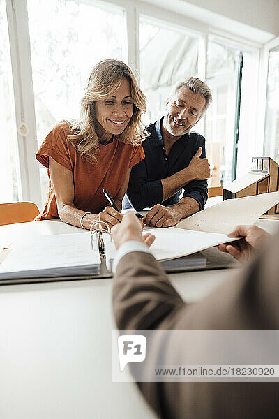 Happy mature woman signing contract with real estate agent at table
