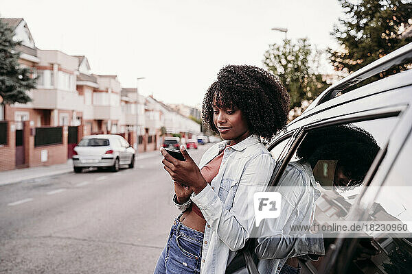 Woman using smart phone leaning on car