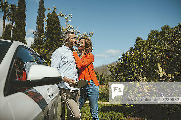 Smiling mature woman standing with man by car on sunny day