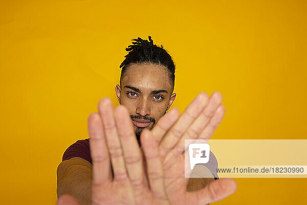 Young man gesturing against yellow background