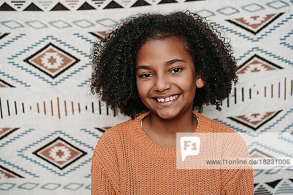 Happy girl with curly hair in front of patterned backdrop