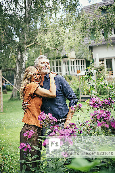 Happy woman hugging man standing by flowering plants