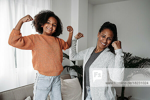 Happy mother and daughter flexing muscles at home