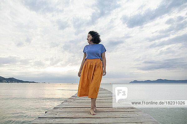 Thoughtful woman walking on jetty in front of sky