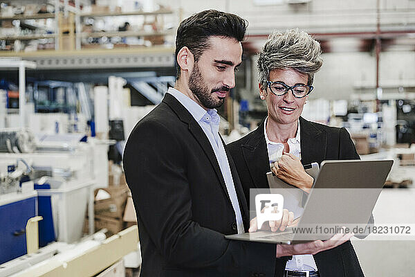 Happy mature businessman discussing with colleague over laptop in industry