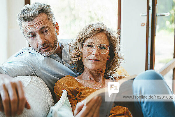Mature woman and man reading book together at home