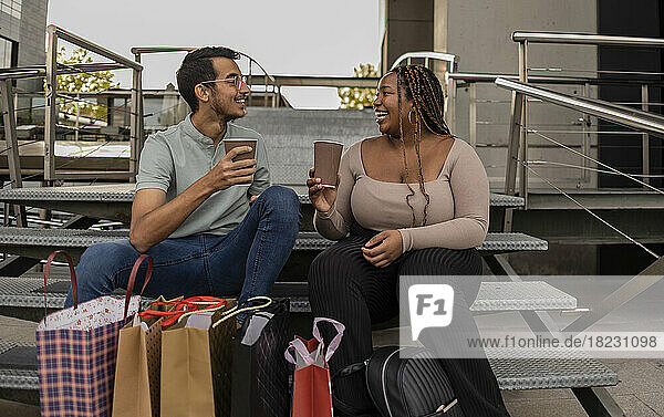 Junges Paar mit Einkaufstüten und Kaffeetassen sitzt auf Stufen