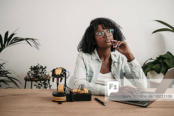 Thoughtful businesswoman with laptop and robot model at home office