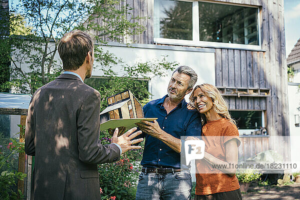 Happy woman and man discussing over model house with real estate agent