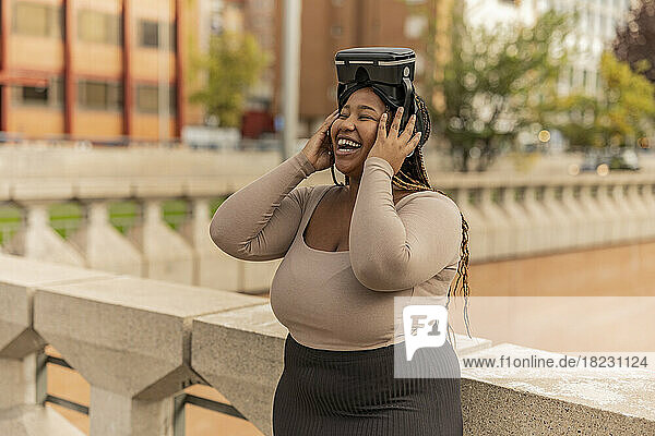 Woman laughing with virtual reality simulator standing by railing