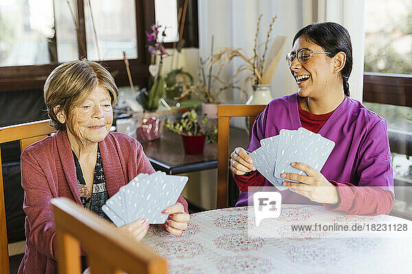 Happy healthcare worker playing cards with senior woman at home