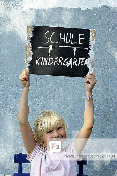 Portrait of little girl holding aloft chalkboard