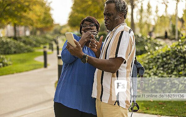 Senior woman laughing by man holding smart phone at park