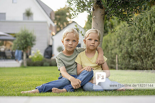 Junge sitzt mit Arm um Schwester auf Gras im Garten