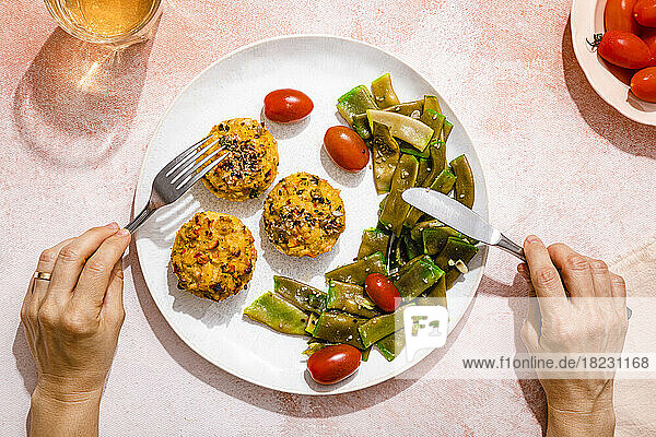 Personal perspective of woman eating rice muffins with cherry tomato and green bean salad