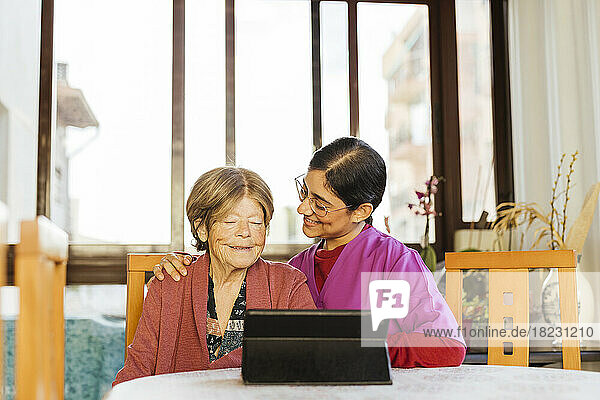 Happy caregiver with senior woman using tablet PC at home