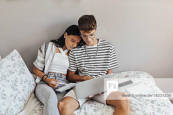 Girl studying with brother on laptop in bedroom at home