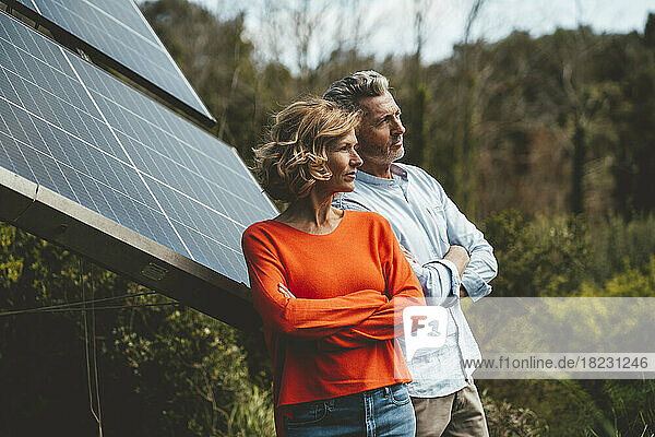 Mature man and woman standing with arms crossed by solar panels