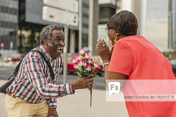 Senior man surprising woman with bunch of flowers