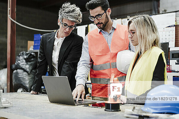 Engineer with colleagues discussing over laptop at industry