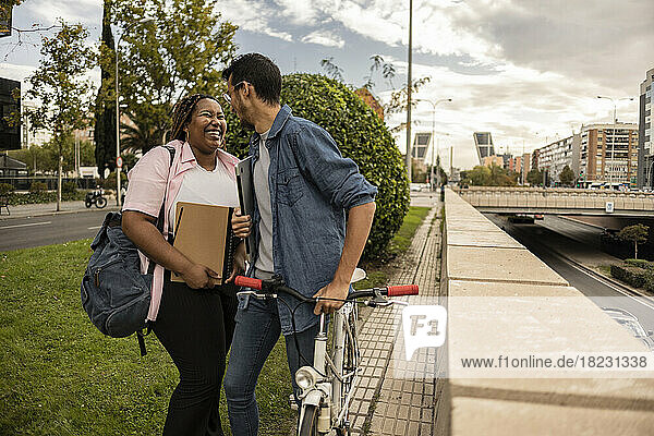 Junges Paar lacht und steht mit Fahrrad am Fußweg