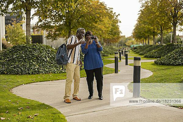 Woman photographing with camera standing by man on footpath in park