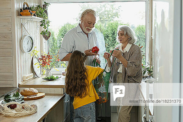 Grandparents and granddaughter unpacking fresh groceries in kitchen