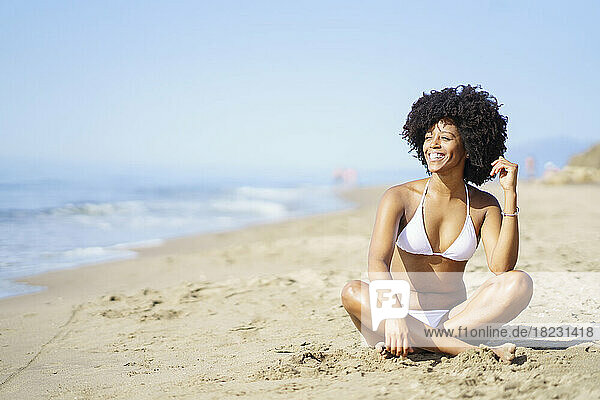Glückliche junge Frau sitzt im Sommer auf Sand am Strand