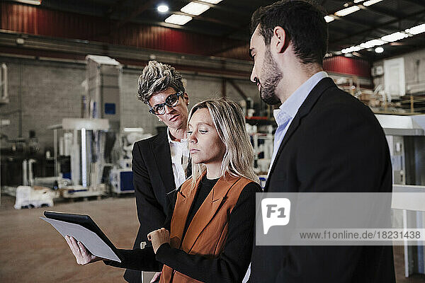 Young businesswoman discussing over tablet PC with colleagues at industry
