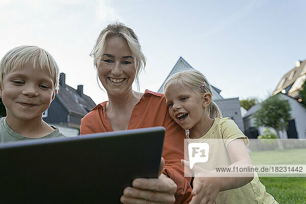 Happy woman sharing tablet PC with children in back yard