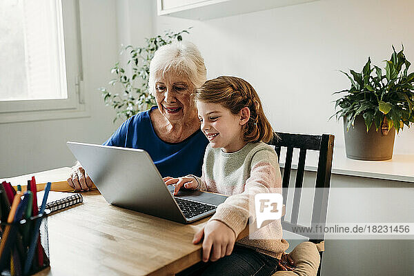 Grandmother helping granddaughter e-learning through laptop at home