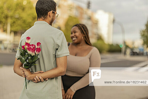 Young man standing with bouquet of flowers in front of woman at footpath