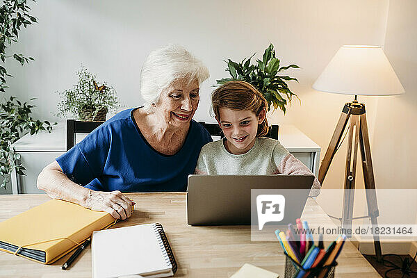 Smiling senior woman helping granddaughter studying through laptop on table at home