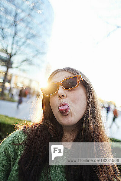 Young woman wearing sunglasses sticking out tongue in front of bright clear sky