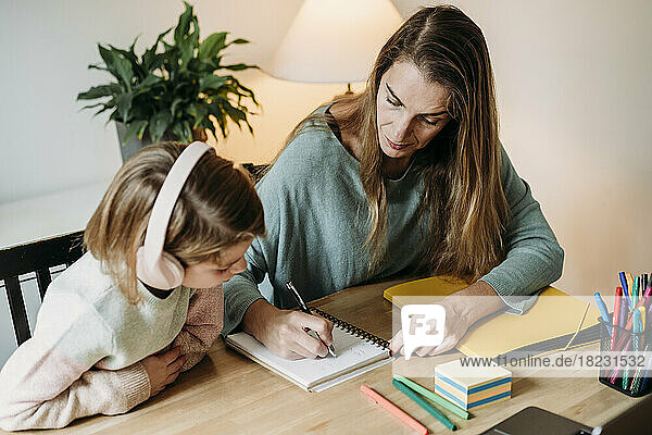 Woman writing on notebook by girl at home
