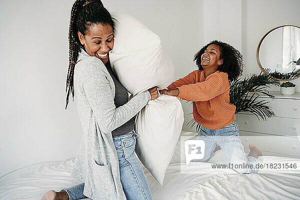 Cheerful mother and daughter playing with pillows on bed at home