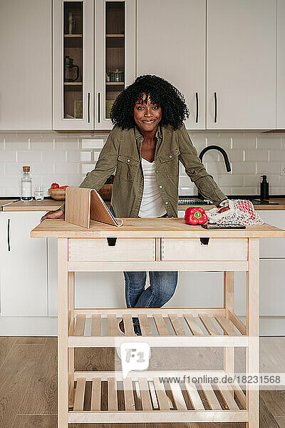 Lächelnde Frau mit Tablet-PC und Netztasche auf der heimischen Kücheninsel