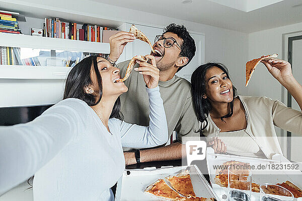Glückliche junge Frau macht ein Selfie mit Frau und Mann  die zu Hause Pizza essen